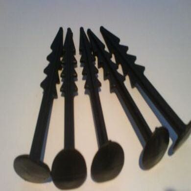Five black plastic stakes with barbed edges are arranged side by side on a light surface, with their flat heads facing the camera.