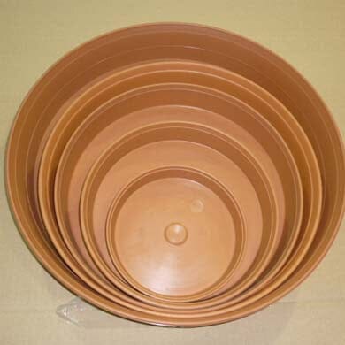 A set of seven round, brown plastic plant pot saucers nested inside each other, shown from above on a beige surface.