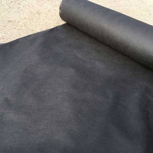 A roll of black landscaping fabric is partially unrolled on a concrete surface, displaying its texture and coverage.
